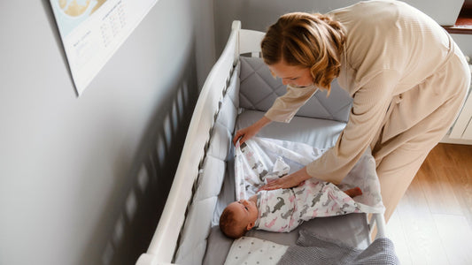 Mother wrapping baby in a swaddle blanket in a crib