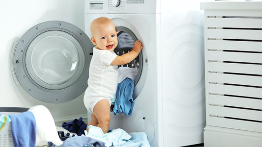 Baby standing in front of a clothes washer making a mess